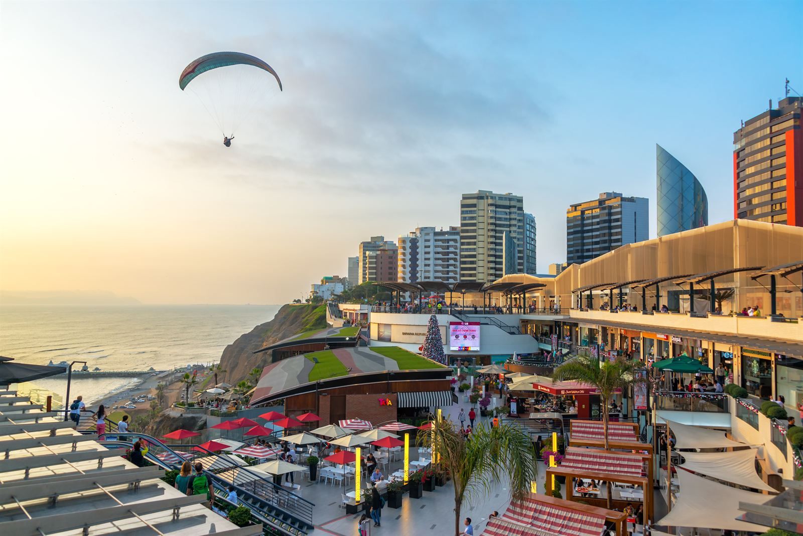 Paraglider over the clifftop shopping terrace and Pacific shoreline in Miraflores, Lima, at sunset