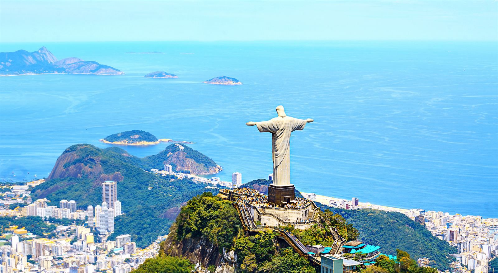 Christ the Redeemer statue with arms outstretched above Rio de Janeiro, with high-rises and offshore islands in the Atlantic