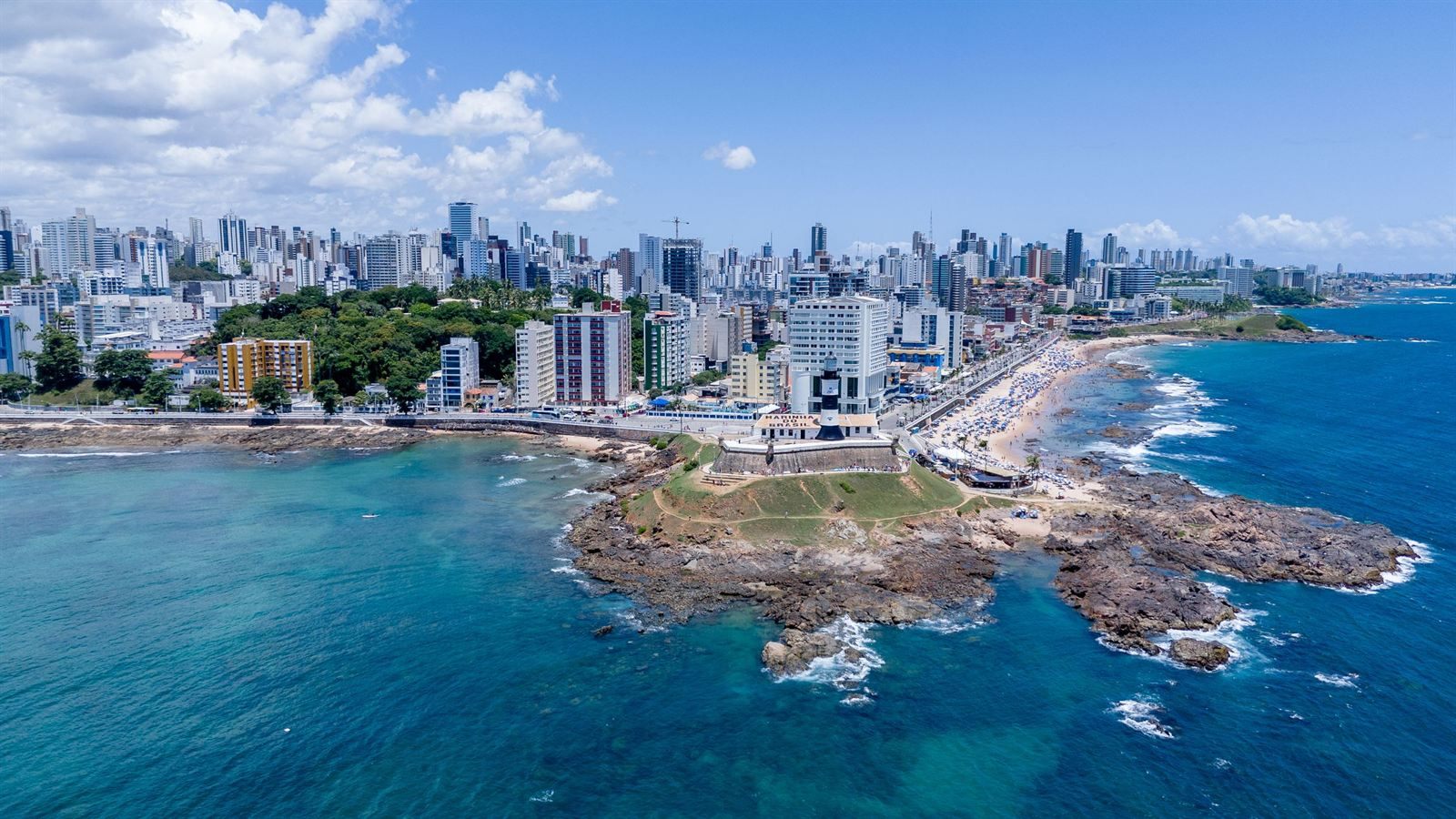 Aerial view of Salvador da Bahia with a seafront fort on a rocky point, turquoise water and a city beach